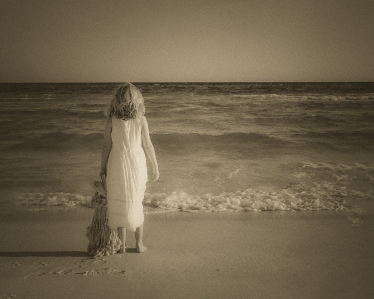 A young girl with her Raggedy Ann doll watching dolphins from the edge of the sea
